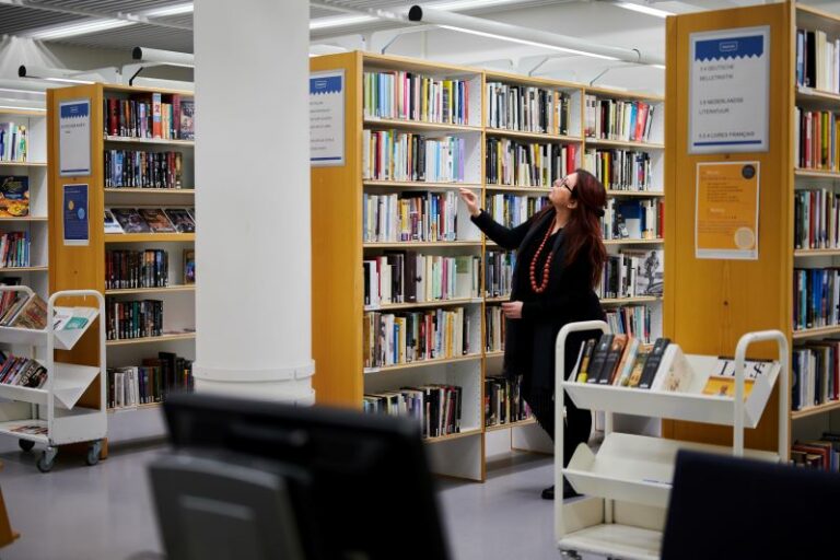 Työntekijä katsoo kirjoja kirjaston hyllyjen välissä